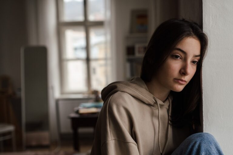 Unhappy teenage girl sitting in home and looking out of window.