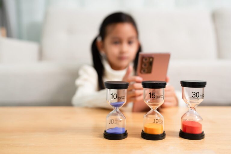 The sand clock with difference time in the background of little girl playing the smartphone.